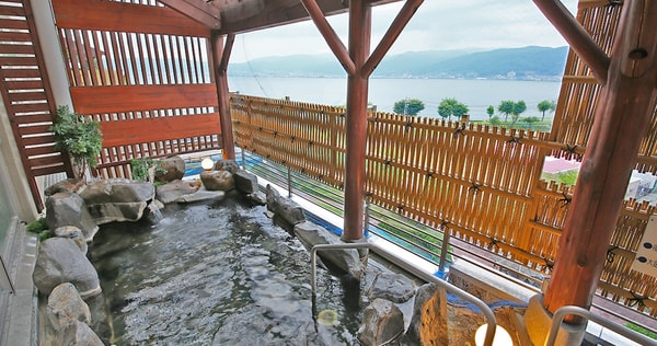 大浴場　露天風呂　八ヶ岳より切り出した大ぶりの岩で設えられた、諏訪湖を一望する露天風呂。日の入り前には夕陽色に染まる湖面を愉しめる