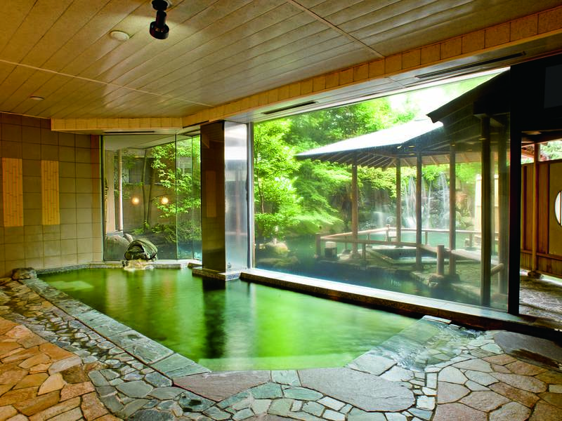 【象山の湯/男性大浴場】大きなガラス越しに庭園と滝を望む、明るく開放感あふれる大浴場